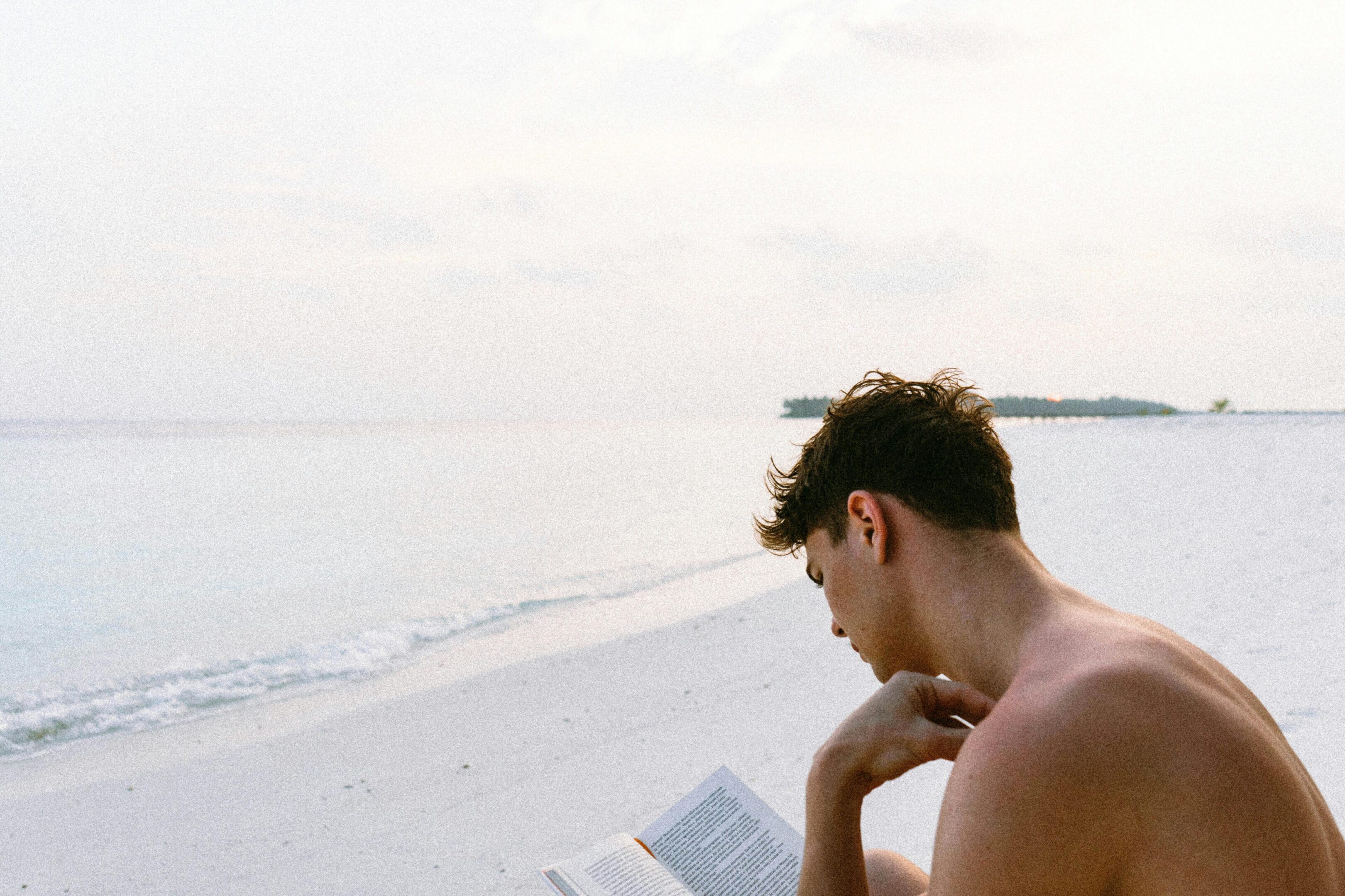 A man sitting on the beach reading a book.