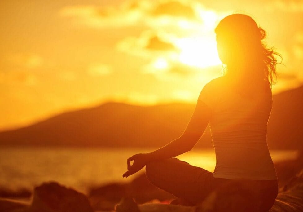 A person sitting in the sun with their hands in yoga pose.