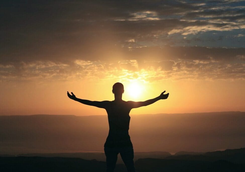 A person standing in front of the sun with their arms outstretched.